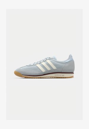 Jasnoniebieskie zamszowe sneakersy z białymi trzema paskami, gumową podeszwą i teksturowaną siateczką. Posiadają gładki czubek oraz logo na pięcie.