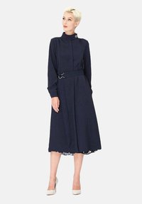 Robe longue bleu marine à manches longues avec un col haut, une taille ceinturée et une jupe évasée. Présente un tissu texturé et un design d'ourlet superposé.