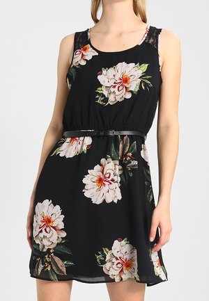 Robe noire avec un grand imprimé floral blanc et rose, sans manches, taille élastique et une fine ceinture, dotée d'accents en dentelle sur les épaules.