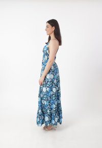 Robe maxi florale avec un motif de roses bleues et blanches, bretelles spaghetti et une jupe fluide avec un ourlet en dentelle.
