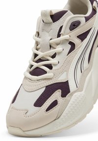 White and purple sneakers featuring a mix of mesh and suede materials, with a textured sole and curved design accents.