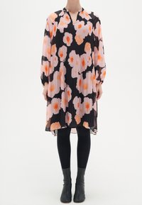 Plisserad klänning med ett rosa och svart blommönster med orange accenter. Långa ärmar, V-ringning, flödande siluett, genomskinligt tyg.