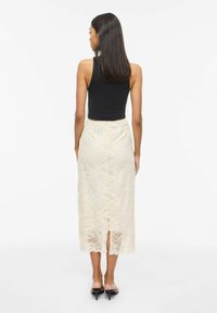 Jupe midi en dentelle crème avec motif floral et fentes à l'ourlet, portée sur un débardeur noir ajusté. Texture lisse, longueur sous le genou.