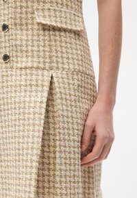 Kreemi tweed kleit tekstuuriga hundihammaste mustriga, millel on lõhikute detail ja mustad nupud liibuva rinnaosa peal.