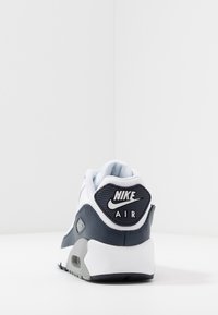 Zapatilla Nike Air con un upper predominantemente blanco y azul marino, materiales de malla y cuero, forma redondeada y una lengüeta trasera texturizada en negro.