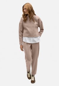 Sudadera de forro polar rosa claro con hombros caídos, combinada con pantalones ajustados a juego y zapatillas de leopardo, superpuesta sobre una camisa blanca.