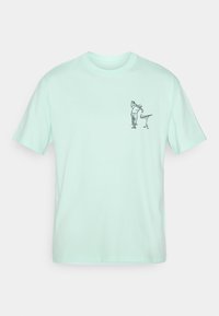 Mintgrøn bomulds t-shirt med korte ærmer. Har en lille sort grafisk illustration på venstre bryst. Standard crew neck design.