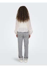 Blusa bianca in pizzo con maniche a sbuffo, vita peplum, abbinata a jeans grigi chiari e sneakers bianche, vista da dietro.
