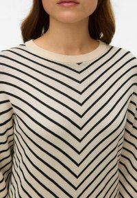 Maglione crema con strisce a chevron nere, texture lavorata a maglia, scollo ampio a coste e vestibilità rilassata. Focus sul motivo e sul contrasto di colori.