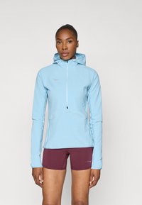 Sweatshirt azul claro com fecho éclair, acabamento texturizado, capuz ajustável e detalhes refletivos, combinado com calções bordô.