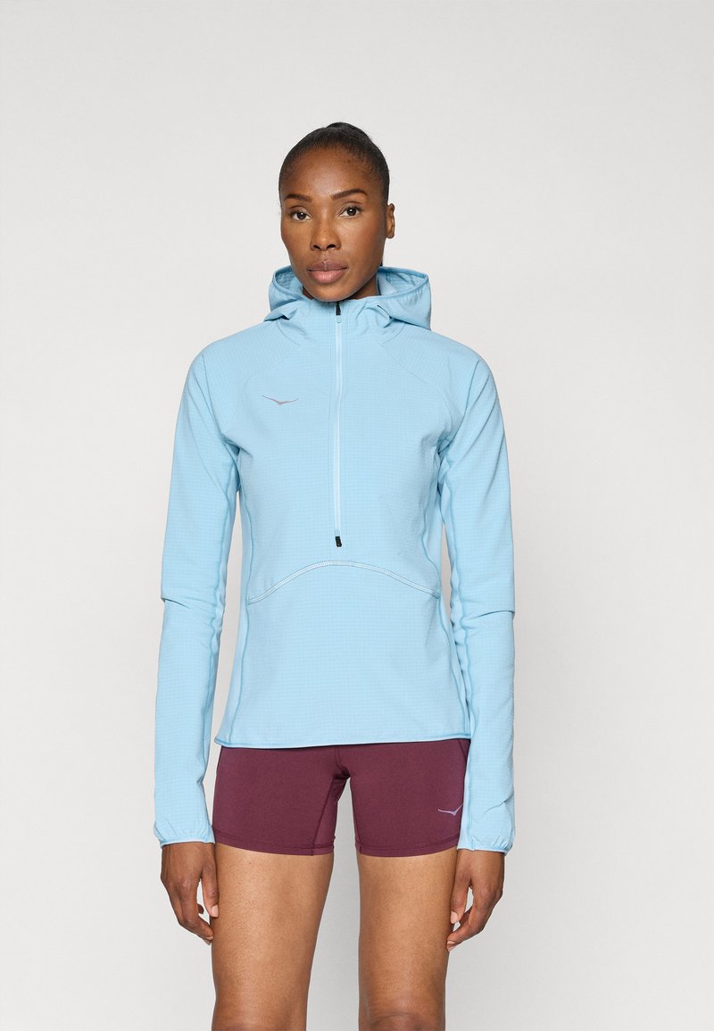 Sweatshirt azul claro com fecho éclair, acabamento texturizado, capuz ajustável e detalhes refletivos, combinado com calções bordô.