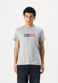 Pilkos spalvos medvilnės marškinėliai trumpomis rankovėmis, su stačiakampio formos logotipu mėlyna ir raudona spalvomis, kuriame yra užrašas "Tommy JEANS". Laidumo stilius, apvali iškirptė.
