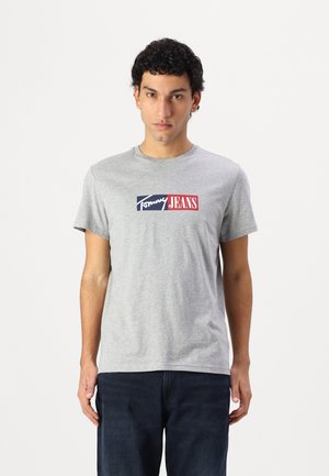 Hallikas puuvillane t-särk lühikeste varrukatega, millel on sinine ja punane ristkülikukujuline logo koos tekstiga "Tommy JEANS". Mugav lõige, ümmargune kaelus.