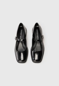 Zapatos Mary Jane de charol negro con punta cuadrada, tira al tobillo y tacón bajo. Textura suave y diseño minimalista.