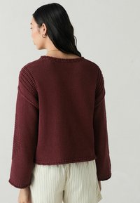 Burgundy stickad tröja med långa ärmar, med en texturerad design och ribbad sömnad längs halsringningen och nederkanten.