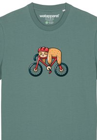 Teal katoenen t-shirt met een cartoonluiaard op een rode fiets met een helm. Eenvoudig ontwerp met heldere kleuren en speelse graphics.