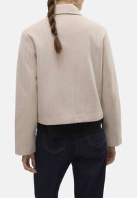 Veste cropped en chevrons rose clair avec une taille côtelée noire et un col à revers, dotée de manches longues et de détails de design minimalistes.