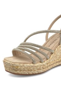 Sandalo con zeppa dotato di una morbida soletta in pelle beige e suola in juta textured, caratterizzato da cinturini metallici incrociati decorati con piccoli ornamenti.