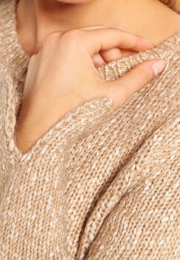 Pull en tricot beige avec un motif texturé, doté d'un décolleté en V et de manches amples. Gros plan sur une main reposant sur l'épaule.