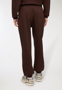 Brązowe dresy z elastycznym pasem w talii i mankietami na kostkach, wykonane z miękkiego materiału, z luźnym krojem i minimalnymi detalami.