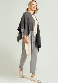 Grå og beige poncho lagdelt over en cremefarvet sweater, kombineret med grå bukser og sølvfarvede sneakers, med en blød, strikket tekstur.