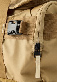 Τσαντάκι από ύφασμα σε μπεζ χρώμα με μαύρη πλαϊνή πόρπη και μερικώς ανοιχτό κατακόρυφο φερμουάρ με μπεζ τριχρωμία.