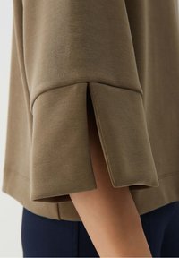 Grön tröja med avslappnad passform, med en design med delade manschetter. Tillverkad av mjukt material med en slät textur och minimalistisk stil.