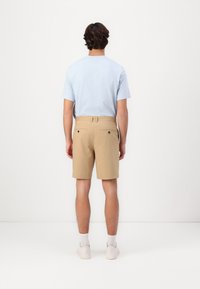 Cămașă scurtă de culoare albastru deschis, cu guler rotund, purtată cu pantaloni scurți bej, care au două buzunare la spate, și teniși de culoare deschisă.