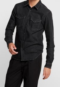 Zwarte spijkerbutton-up shirt met twee borstzakken, lange mouwen en een gebogen zoom. Kenmerkt zich door contrasterende stiksels en een klassieke kraag.