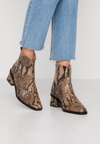 Botines con estampado de serpiente en marrón y negro, punta afilada, tacones bloque, combinados con unos pantalones vaqueros de mezclilla celeste recortados.