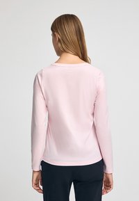 Långärmad skjorta i ljusrosa tyg med rund halsringning och mjuk textur. Bakifrån visar den en enkel design med en kurvad fåll.