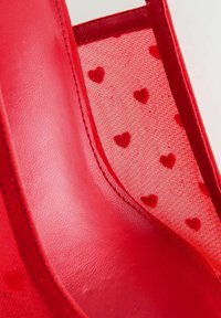 Material din piele roșie alături de țesătură din plasă roșie cu modele mici de inimioare roșii, evidențiind cusăturile detaliate și textura.