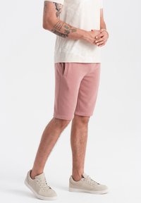 Růžové šortky z bavlněného směsového materiálu se bočními kapsami, volným střihem a měkkou strukturou, doplněné béžovými teniskami.