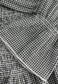 Mustvalge ginghami kangas nähtavate õmbluste ja omavahel üksteise peale õmmeldud osadega, näidates üksikasjalikku tekstiili tekstuuri ja mustrit.