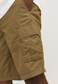 Shorts cargo kaki en coton, avec de grandes poches latérales, des coutures cousues et une texture légèrement froissée. Hauteur de taille standard.