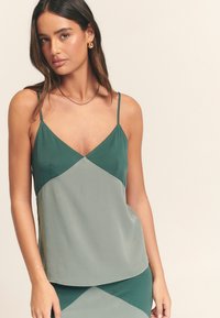 Saténová kamizolka v tmavozelenej a svetlozelenej farbe, s výstrihom do V a tenkými ramienkami, hladkej textúry a diagonálnym farebným blokovaním.