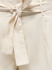 Gros plan d'un pantalon en tissu beige avec un nœud de ceinture noué à la taille et des détails de couture visibles.