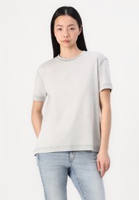 Camiseta de manga corta gris claro con escote redondo y corte relajado, hecha de una tela suave, con detalles de costura. Combinada con jeans azules.