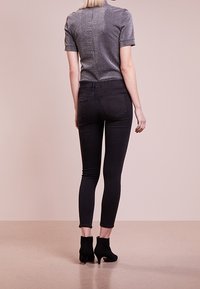 Top gris ajustado de manga corta, combinado con jeans ajustados negros y botines negros. Tela suave con un ligero brillo, diseño entallado.