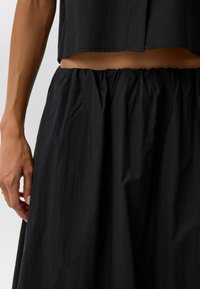 Zwarte cropped top met een losse pasvorm en rok met elastische tailleband. De stof heeft een licht verhoogde textuur, wat de eenvoud van het ontwerp benadrukt.