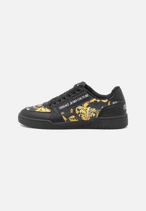 Sneaker nera con un design floreale giallo, realizzata in materiale sintetico morbido, punta rotonda e chiusura con lacci. Logo bianco "Versace Jeans Couture".