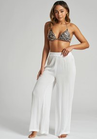 Bikini w trójkątnym topie w panterkę zestawiony z białymi, lekkimi, zwiewnymi spodniami o szerokich nogawkach. Spodnie mają elastyczny pas i miękką strukturę.