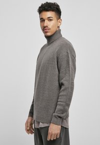 Suéter gris de punto con cuello alto, puños acanalados y un acabado texturizado, usado sobre una camiseta interior de color gris claro en capas.