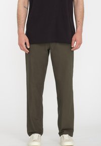 Olijfgroene katoenen broek met een rechte pasvorm, voorzien van riemlussen en zijzakken, gedragen met witte sneakers.