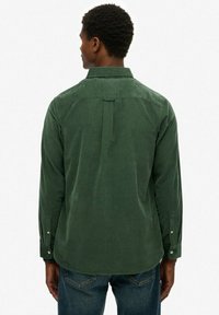 Groen corduroy overhemd met een button-down kraag, rugplooi en lange mouwen, voorzien van knopen bij de boorden en een gladde textuur.
