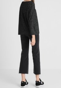 Svart och grå långärmad tröja med avslappnad passform, kombinerad med högmidjade svarta cropped jeans och svarta sportskor med vita sulor.