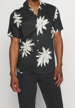 Chemise noire à manches courtes avec un motif floral blanc, à col et fermeture à boutons. Le tissu semble léger avec une texture douce.