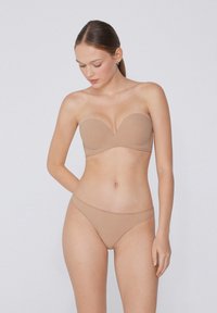 Podprsenka bez ramínek v tělové barvě s výstřihem ve tvaru srdce, hladkým povrchem a odpovídající tělovou tanga. Jednoduchý, bezšvový design bez viditelného kovového prvku.