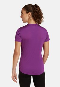 Camiseta de manga corta morada con cuello redondo, textura suave y diseño ajustado, combinada con pantalones negros, vista desde atrás.