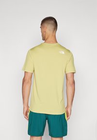 Šviesiai geltona trumpomis rankovėmis marškinėliai su apvaliu kaklu, ant viršutinės nugaros dalies turi nedidelį baltą logotipą. Dėvimi su žalsvai mėlynomis šortais.